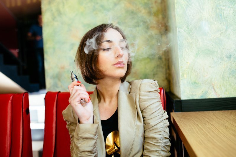 Mujer vapeando con un cigarro electrónico en la mano