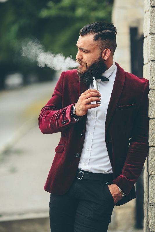 Hombre en esmoquin guinda vapeando con un cigarro electrónico SMOK